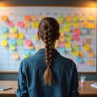 Young woman plans social media content. She stands by board with color sticky notes. Female uses visual schedule for planning tasks and workflow.