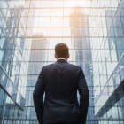 Back of businessman in suit with business office glass modern buildings background for financial freedom portfolio or company profit and strategy growth IPO poster
