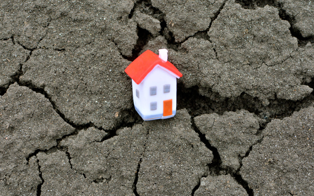 Photo d'une petite maison en papier sur fond de terre craquelée