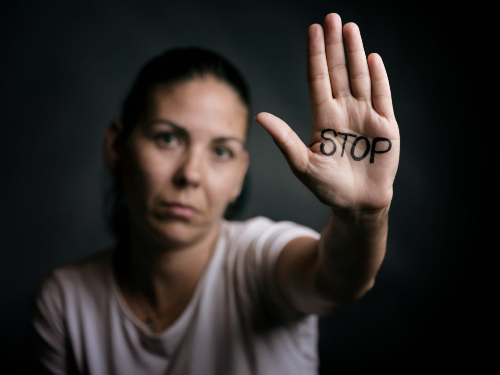 Photo d'une femme qui brandit sa main sur laquelle est écrit STOP, illustrant le harcèlement, la violence