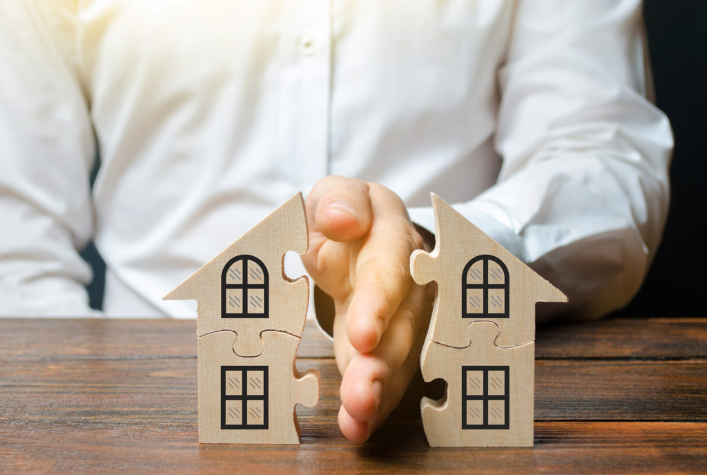 Maison en pièce de puzzle en bois avec une main d'homme la séparant en deux