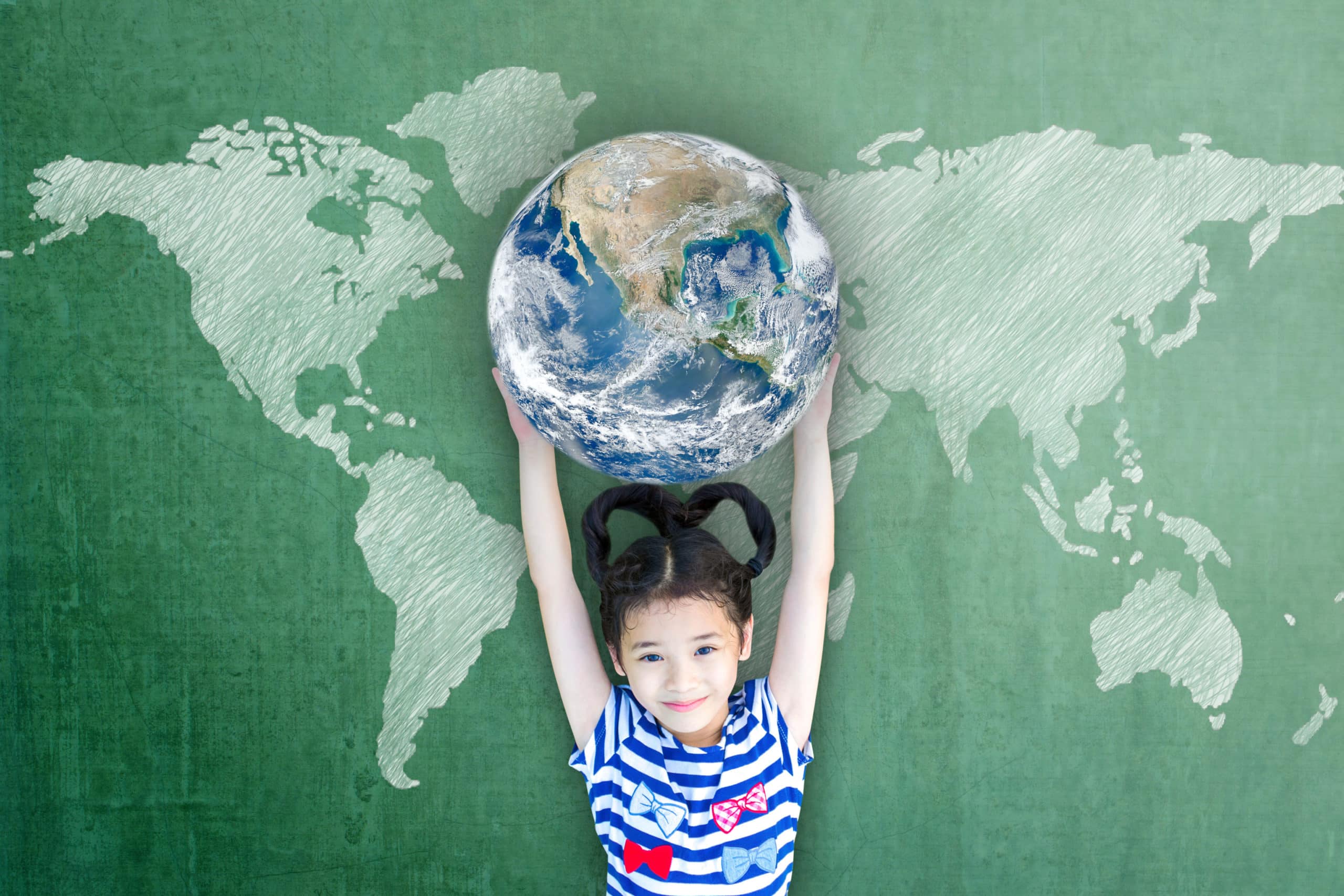 Fille qui tient au dessus de sa tête bras tendus une mappemonde devant un tableau d'école sur lequel figure une mappemonde