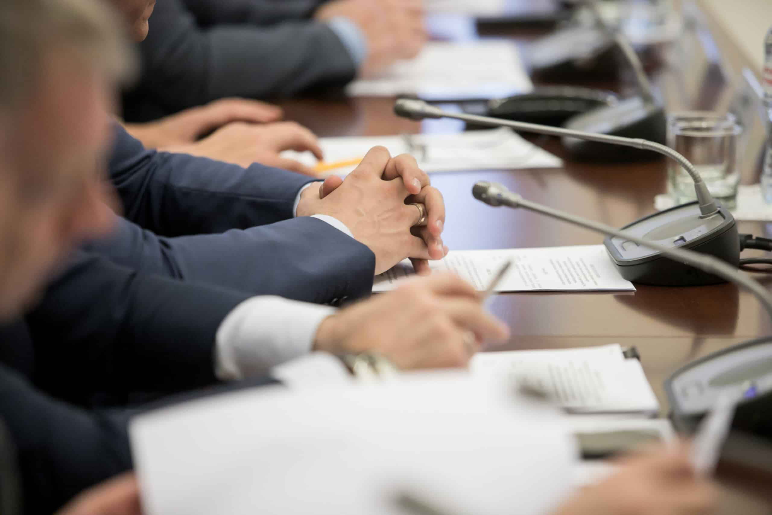 One of politician sitting by table with his hands over document during political summit or conference